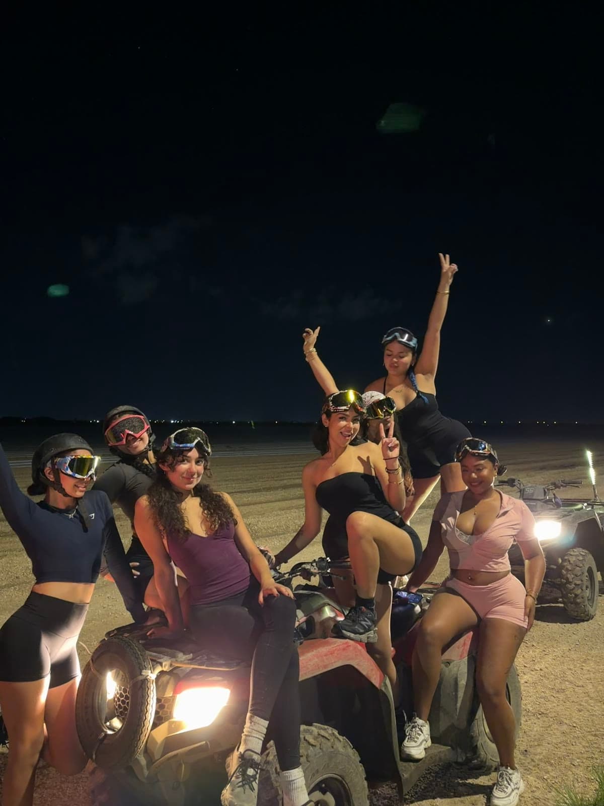 A group on lit ATVs after dark, arms in the air
